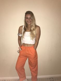 a woman standing in front of a wall wearing an orange pants and white tank top