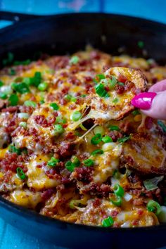 a person scooping food out of a skillet with green onions and other toppings