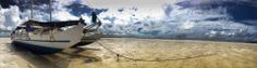 a boat sitting on top of a sandy beach next to the ocean with clouds in the sky