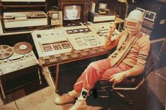 a man sitting in a chair next to a table full of sound equipment and recording equipment