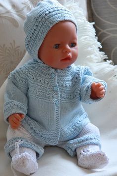 a small baby doll sitting on top of a white couch wearing a blue knitted outfit