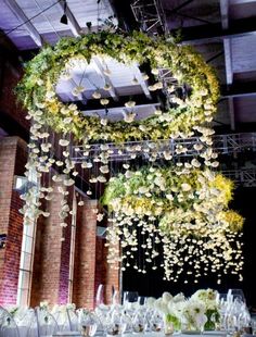 an arrangement of flowers and greenery is suspended from the ceiling at a wedding reception