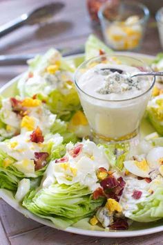 a white plate topped with lettuce and salad next to a small bowl of dressing