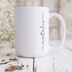 a white coffee mug sitting on top of a wooden table next to a vase with baby's breath