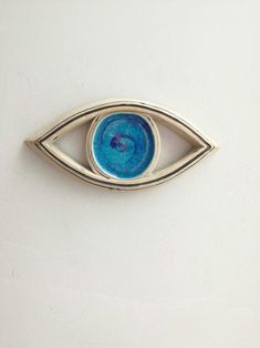 a brooch with an eye on it is sitting on a white surface in front of a wall