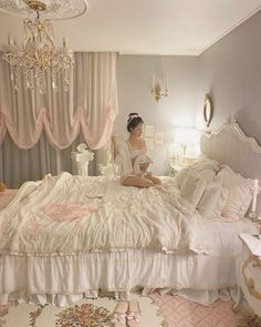 a woman sitting on top of a white bed in a bedroom next to a chandelier