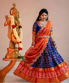 a woman in an orange and blue lehenga standing next to a gold statue