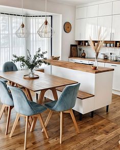 a kitchen with white cabinets and blue chairs in front of a wooden dining room table