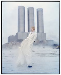 a woman standing in front of some silos wearing a white coat and black boots