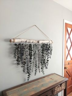 a wooden table sitting in front of a wall hanging with leaves and branches on it