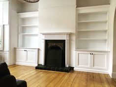 an empty living room with white bookcases and a fireplace