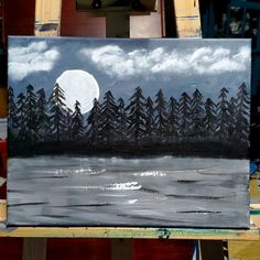 an easel with a painting on it that has trees and the moon in the sky