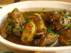 a white bowl filled with meat and potatoes covered in gravy, garnished with parsley