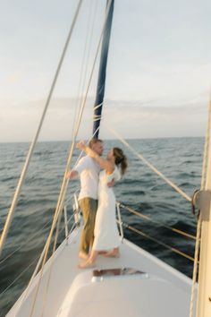 a man and woman standing on the bow of a sailboat in the middle of the ocean