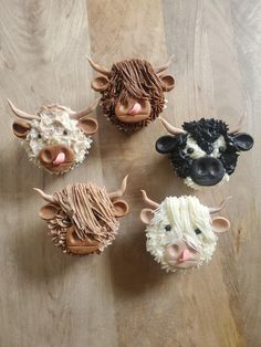 four cupcakes decorated to look like cows on a wooden table with brown and white icing