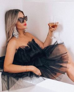 a woman in a black dress sitting on a white chair holding a glass of wine