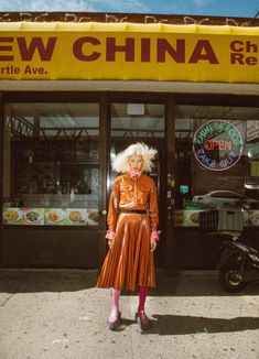 a woman standing in front of a restaurant wearing an orange dress and pink boots with her hair pulled back