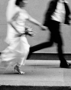 black and white photograph of two people walking down the street, one holding hands with the other