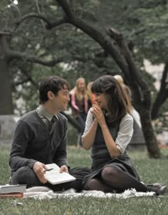 a man and woman sitting on top of a grass covered field next to each other