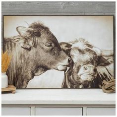 an image of two cows kissing in front of a wooden frame on a shelf with other items