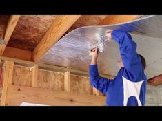 a man in blue jacket working on a metal ceiling fixture with an aluminum sheet over his head