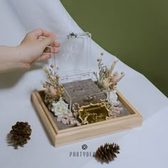 a person is holding up a cake with flowers and pine cones on the table next to it