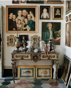 a room with many paintings and pictures on the wall, including an antique console table