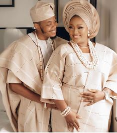 two people standing next to each other in front of a bed wearing white clothing and pearls