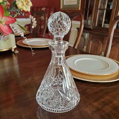 a glass decanter sitting on top of a wooden table next to plates and flowers