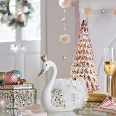 a white swan sitting on top of a table next to a wine glass and christmas tree