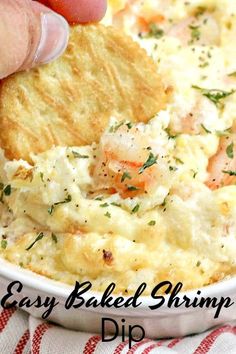 a hand dipping a piece of bread into a casserole dish with shrimp and cheese