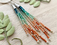 several different colored beads are hanging from a necklace on a table with leaves and flowers