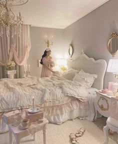 a woman standing in front of a bed with white furniture and pink curtains on the windowsill