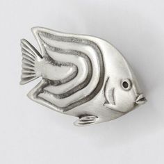 a silver fish brooch sitting on top of a white surface