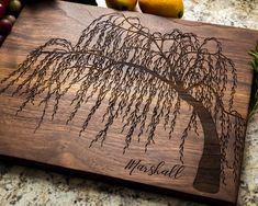 a personalized cutting board with a tree on it and some fruit in the background