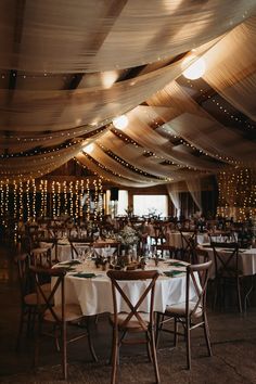 the inside of a tent with tables and chairs set up for a wedding reception under string lights