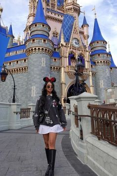 a woman standing in front of a castle with a minnie mouse ears on her head