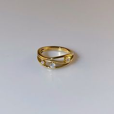 a yellow gold ring with three diamonds on the top and bottom, sitting on a white surface