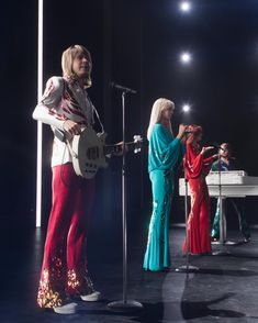 two women in brightly colored outfits are singing and playing instruments while one woman is holding a microphone