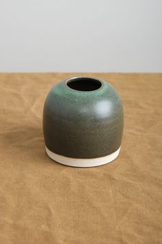 a green vase sitting on top of a wooden table next to a brown cloth covered floor