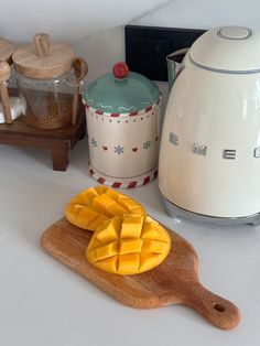 a wooden cutting board topped with sliced mangoes next to an electric kettle and toaster