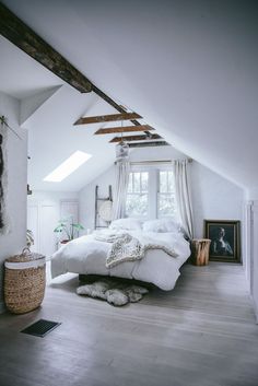 an attic bedroom with white bedding and wooden beams, windows, and rugs on the floor