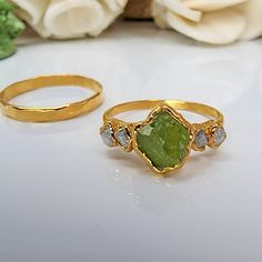 two gold rings with green and white stones on them next to a flower arrangement in the background