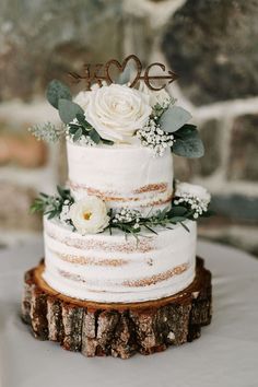 a wedding cake with white flowers and greenery is on top of a tree stump