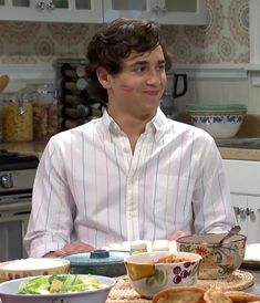 a man sitting at a kitchen table with food on the plate and bowls in front of him