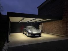 a silver sports car parked in front of a garage at night with its lights on