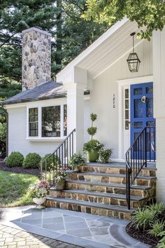 a white house with blue door and steps leading up to the front door is surrounded by greenery