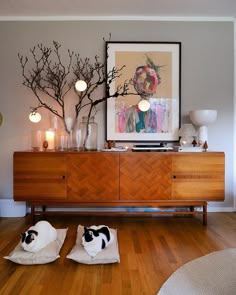 two black and white cats laying on pillows in front of a dresser with art above it