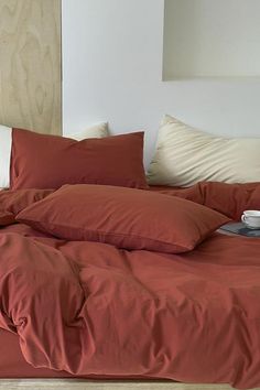 an unmade bed with red sheets and pillows