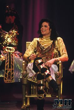 michael jackson sitting in a chair with his feet up on the ground and another man standing behind him